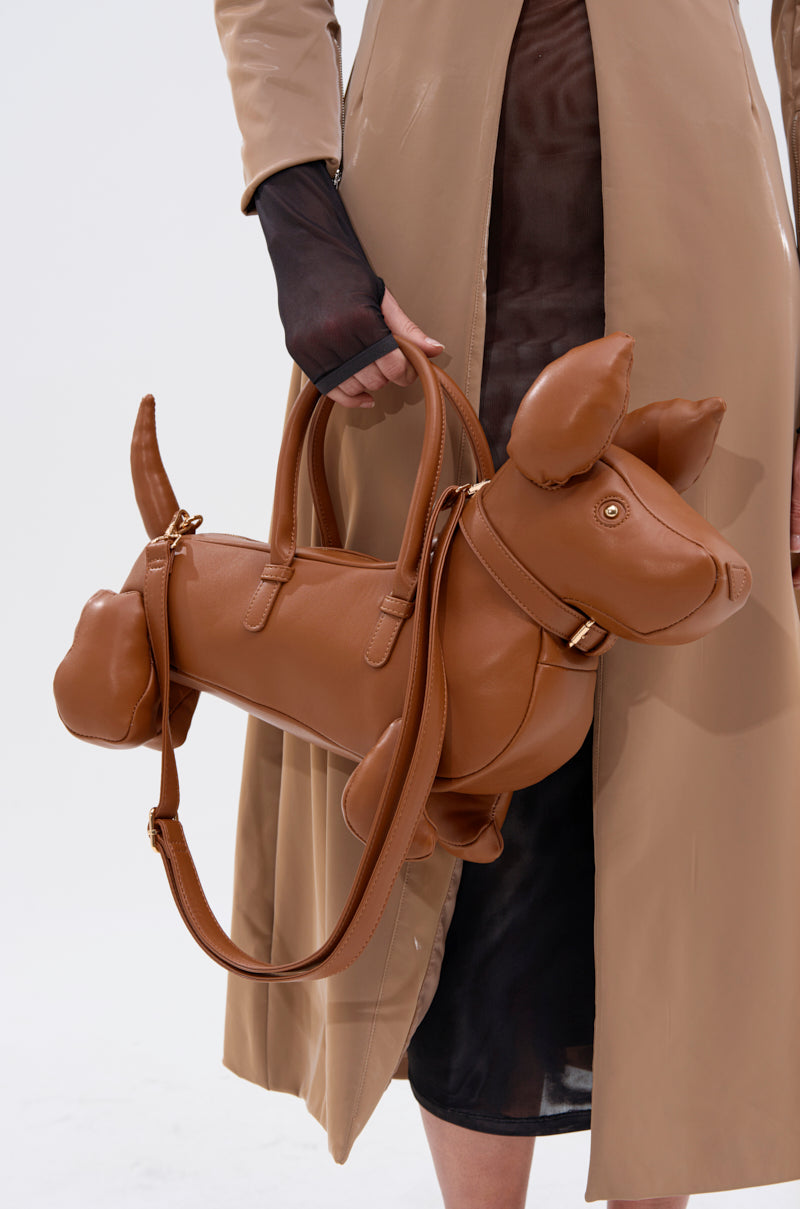 Wearing a beige coat and sheer black dress, a person carries the I'M REALLY A DOG PURSE—a novelty bag shaped like a dachshund with detailed stitching, handles, and a shoulder strap.