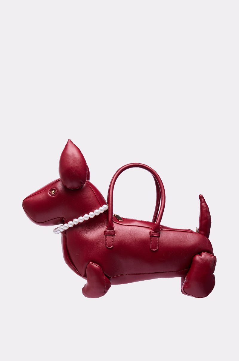 The PRETTY BUT I BITE BACK PURSE is a faux leather, dog-shaped bag in red, featuring a pearl necklace and two handles on its back, displayed against a plain light background.