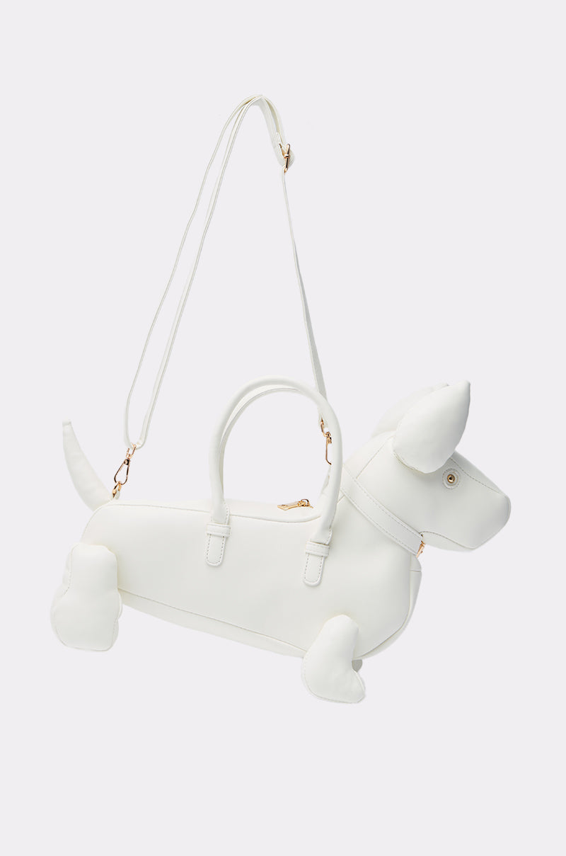 The I BITE PU PURSE is a white dog-shaped bag with floppy ears, a tail, gold hardware, top handle, and detachable shoulder strap—crafted from premium faux leather for a playful look.