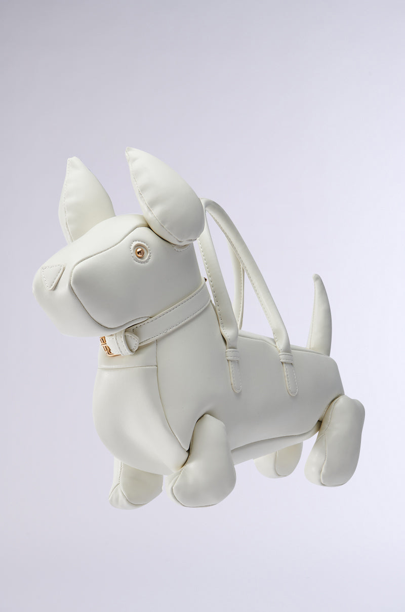 The I BITE PU PURSE is a dog-shaped, faux leather bag resembling a white plush dog with short ears and a wagging tail. It features gold accents, two handles, and includes a detachable shoulder strap against a light gray background.