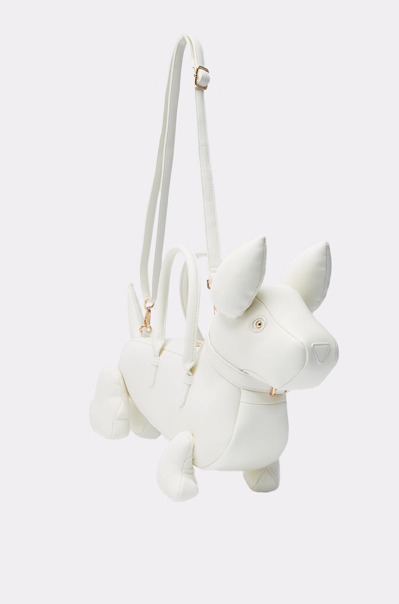 The I BITE PU PURSE is a white, dog-shaped faux leather bag with pointy ears, round eyes, a tail, two handles, and an adjustable detachable shoulder strap for versatile carrying.