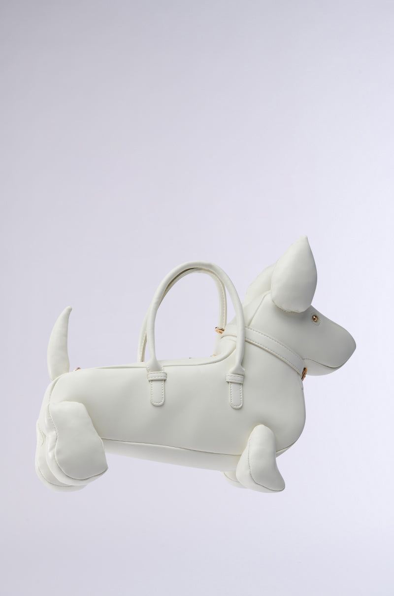 The I BITE PU PURSE is a white faux leather, dachshund-shaped purse with gold hardware. It has detailed ears, legs, tail, and snout. Two handles run along the back, complemented by a detachable shoulder strap for versatility. The background is light gray.