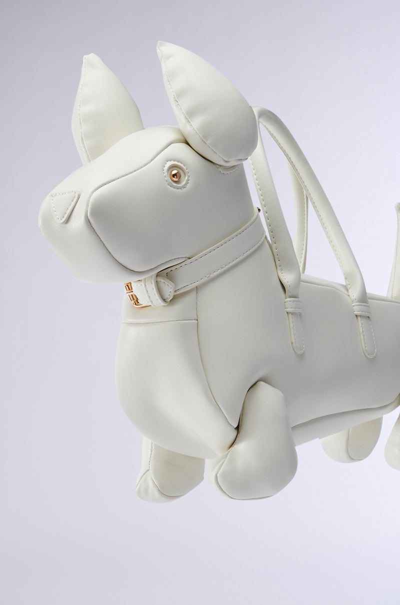 The I BITE PU PURSE is a whimsical dog-shaped purse made of light-colored faux leather. It features pointed ears, a collar with a small buckle, two shoulder straps, and an optional detachable strap, all set against a plain neutral background.