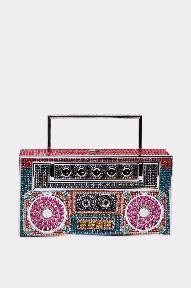 The TURN ME UP BLING BOOMBOX PURSE is a rectangular bag styled like a vintage stereo, featuring colorful rhinestones and a black top handle.