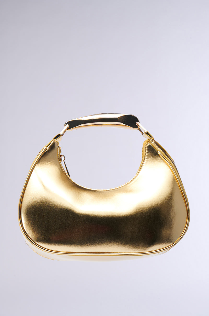The TOP TIER ONLY PU PURSE, featuring a structured crescent silhouette and metallic top handle in a shiny gold finish, stands out against a plain gray background.