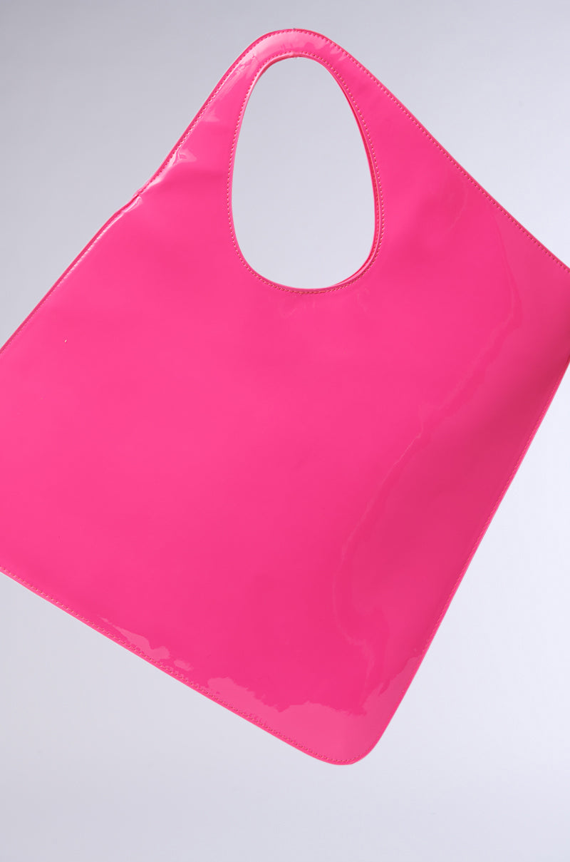 The CHECK ME OUT PURSE is a bright pink, shiny faux patent leather bag with a geometric silhouette and triangular shape, featuring a large oval handle opening, isolated on a plain light background. 4