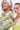 Two women pose together. The older woman, with long gray hair and green earrings, wears a floral jacket and holds the IM OUT HERE BLING PURSE. The younger sports slicked-back hair, layered necklaces, and a strapless lime green brocade top.