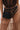 A person wears a sheer, polka-dot beige skirt and black corset top, accessorized with the JACKY BELT BAG—a structured rectangular faux leather bag—attached at the waist.