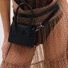A person wears a sheer, polka-dot beige skirt and black corset top, accessorized with the JACKY BELT BAG—a structured rectangular faux leather bag—attached at the waist.