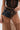 Wearing a sheer brown polka dot skirt and black corset top, a person holds the JACKY BELT BAG—a small faux leather bag with removable shoulder strap—at their waist.