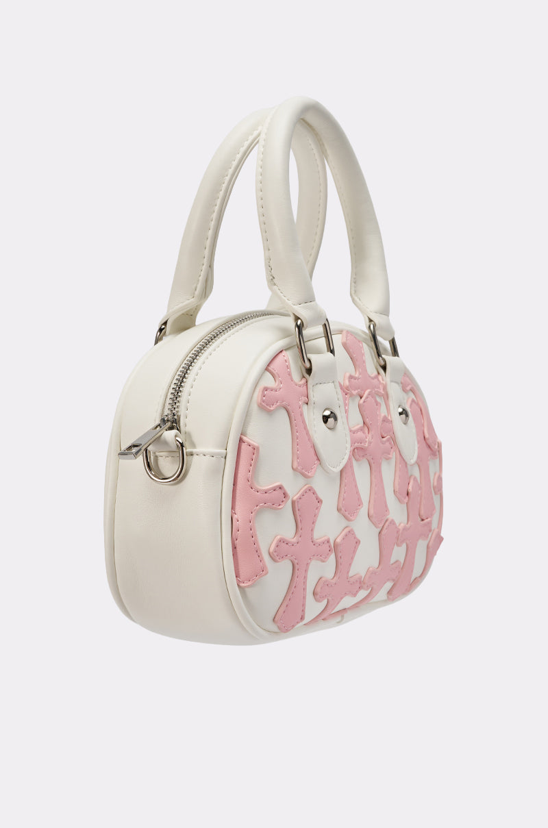The ELLE CROSS PURSE is a white round faux leather handbag with silver hardware, two short handles, pink cross appliqués on the front and side, and a top zipper closure for a stylish look.