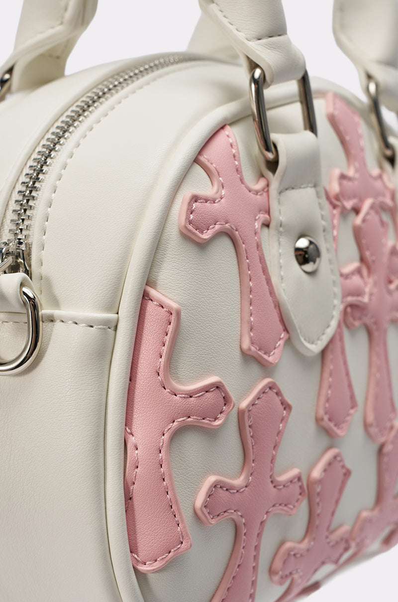 Close-up of the ELLE CROSS PURSE, a white round faux leather bag with silver zipper, pink cross appliqués, and white handles accented by sleek silver hardware for a chic look.