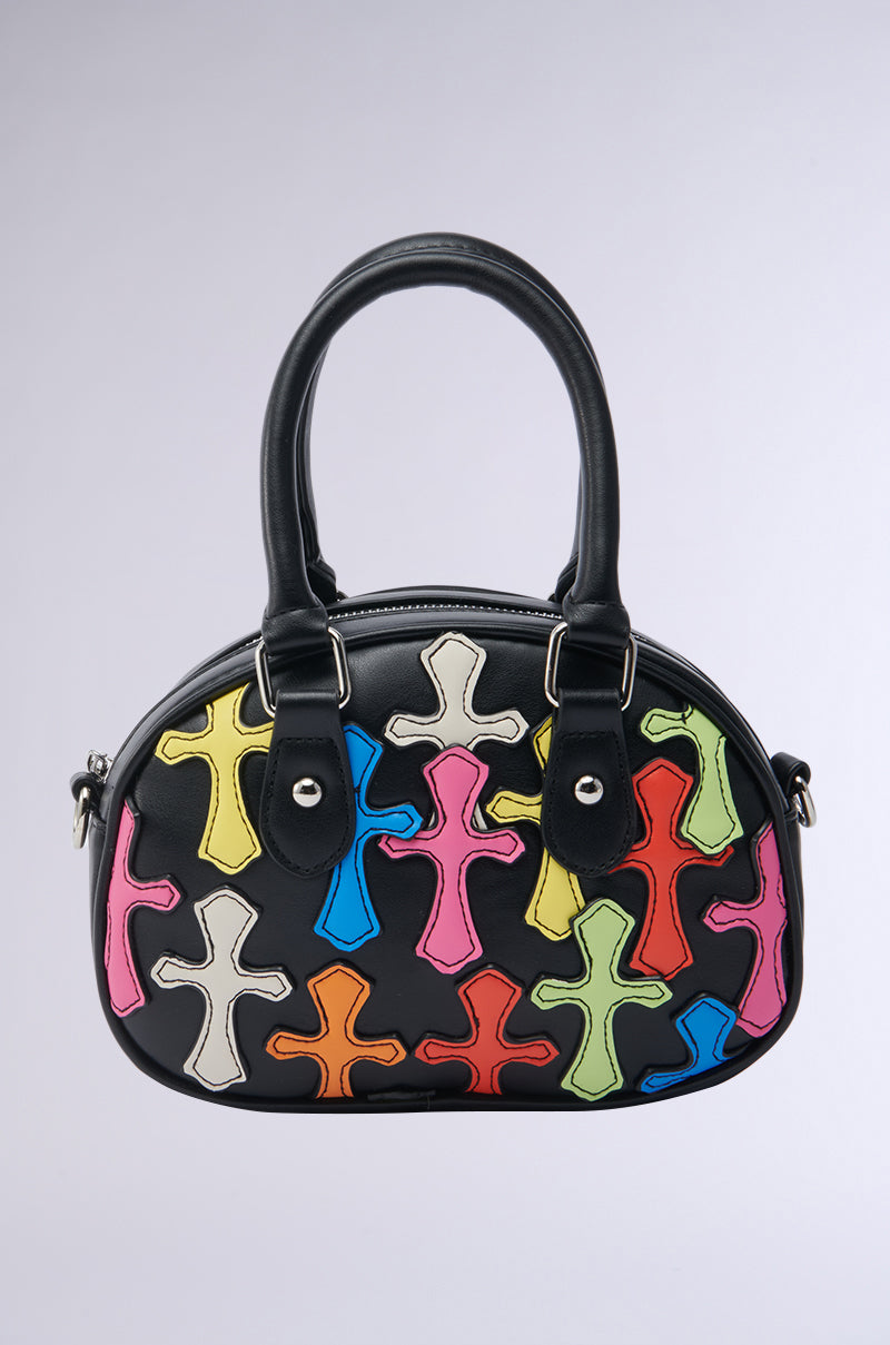 The CROSS ME PATCH PURSE is a black faux leather handbag with two handles, featuring colorful cross-shaped patches in pink, blue, yellow, orange, green, and red on the front. It stands out against a plain light gray background. 1