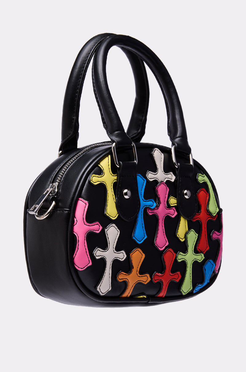 The CROSS ME PATCH PURSE is a black faux leather bag with two handles, featuring colorful overlapping cross-shaped patches in pink, yellow, green, blue, white, and red—ideal for those who love unique cross patch styles. 2
