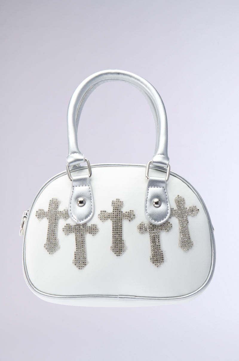 The CROSS MY HEART BOWLING PURSE is a small white handbag crafted from faux leather, featuring double handles and three silver beaded cross designs on the front, all set against a light gray background. It also offers an optional crossbody fit for added versatility, allowing it to effortlessly convert into a chic bowling purse.