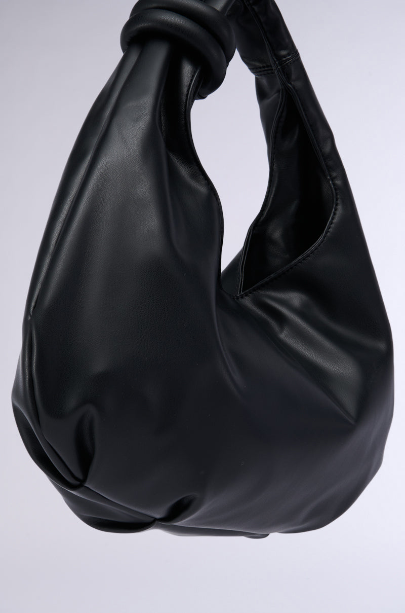 The TOO TRENDY PU TOTE is a modern, black faux leather handbag boasting a smooth, sleek finish and a twisted-handle design. The bag's spacious interior complements its minimalist, elegant appearance. Photographed against a plain light grey background, this chic piece from the AKIRA Label epitomizes timeless sophistication.