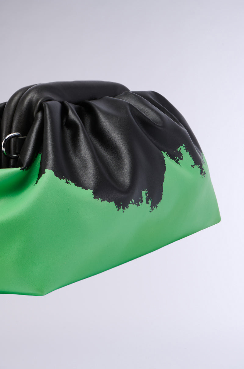 A close-up of the CHOOSE BOTH COLORBLOCK CLUTCH, a faux leather bag with a distinct design. The upper part showcases a black paint-splatter effect that seamlessly blends into the vivid green lower section. This clutch highlights a silver ring detail near the top and comes with a removable strap for added convenience.