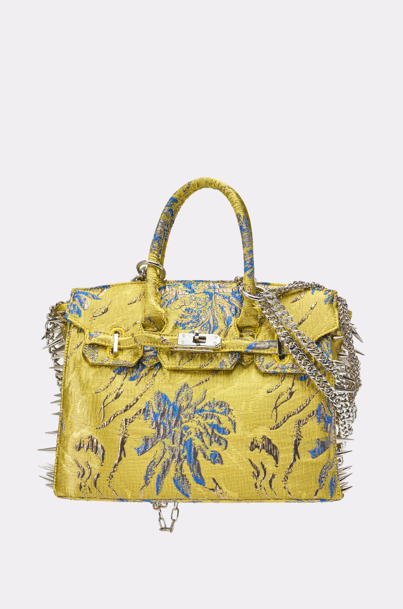 The LETS GO EMBELLISHED TOTE is a yellow handbag with blue floral embroidery, silver spikes on the sides, a top handle, chain shoulder strap, and a silver front clasp.