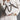 A person in a white suit and lace dress carries the STAY BLESSED SPIKE PURSE, a fashion-forward faux leather bag featuring silver spikes and metal chains for a bold, edgy look.