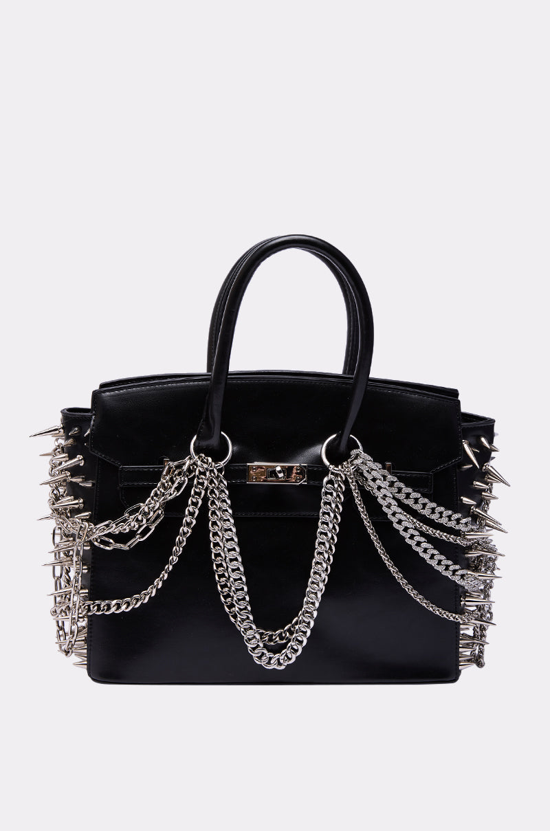 The I BITE BACK EMBELLISHED TOTE is a black faux leather handbag with silver spikes, metal chains, double handles, and a metallic front clasp, shown against a plain light background. 3