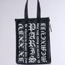 The CHAMPS GRAFFITI PURSE is a black, rectangular tote bag made of faux leather with sturdy handles. The front features bold, white, gothic-style text that reads "PARIS" and various Roman numerals. The bag also has "Charles de Gaulle Étoile Paris" written on the sides in smaller gothic-style text, complemented by subtle graffiti patterning.