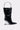 The STEP ON IT PURSE is a black, shiny bag shaped like a pointed-toe boot, featuring a silver metal handle and a transparent wedge-shaped heel, shown on a plain light background.