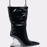 The STEP ON IT PURSE is a black, shiny bag shaped like a pointed-toe boot, featuring a silver metal handle and a transparent wedge-shaped heel, shown on a plain light background.