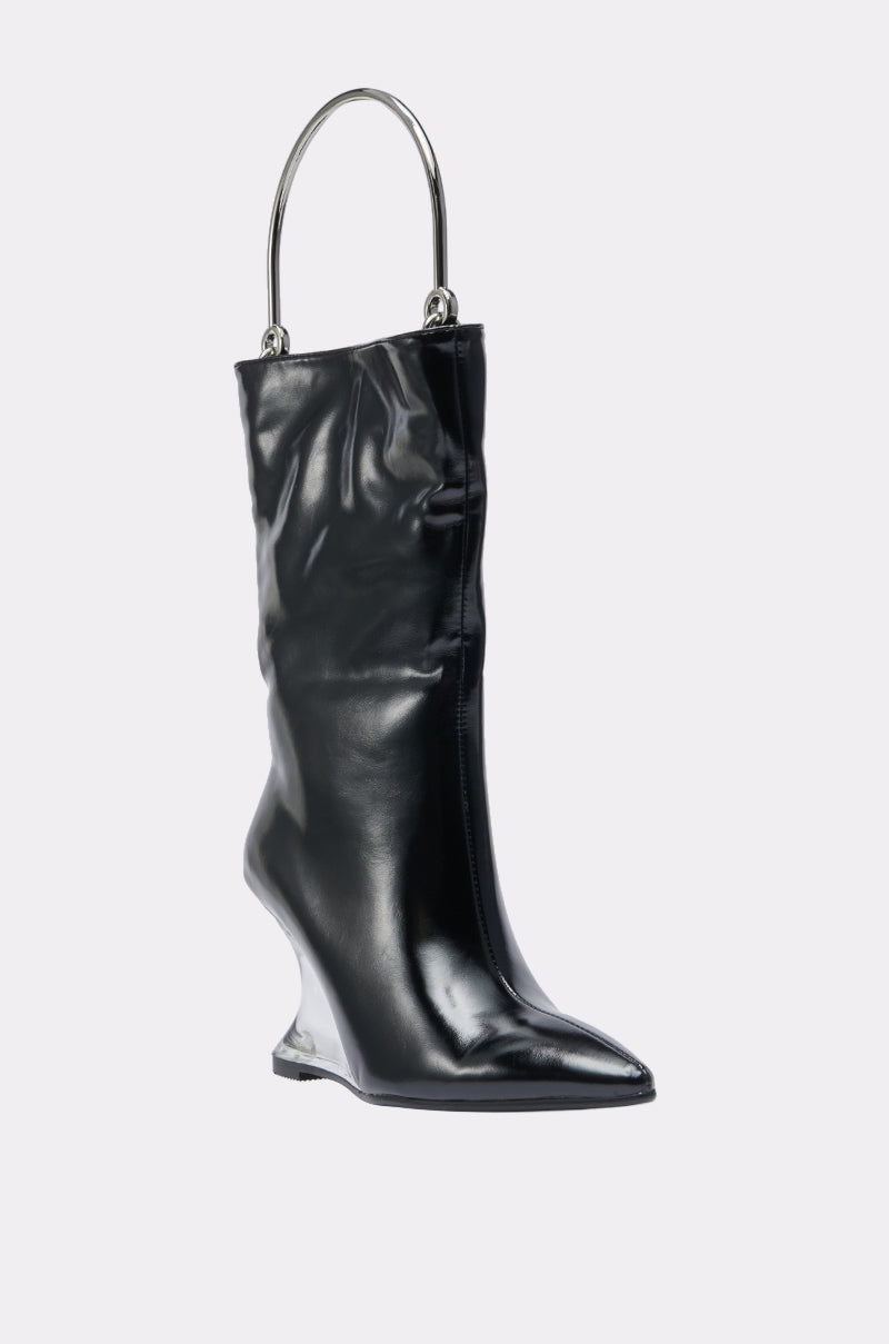 The STEP ON IT PURSE is a unique shiny black high-fashion accessory shaped like a boot, featuring an angular sculpted wedge heel and a large metallic handle at the top, showcased against a plain light background.