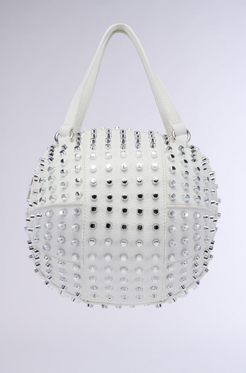 A white faux leather handbag with a spherical shape and two sturdy handles, the STAY BACK SPIKE BASKETBALL BAG is adorned with rows of silver and black metal studs, creating a striking, textured design against a plain light gray background.