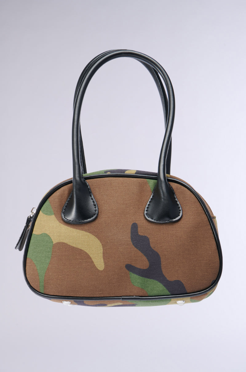 Introducing the KELLY CAMO NIGHTS MINI PURSE, a chic accessory with a small camo print in shades of green, brown, and black. This purse boasts black leather handles and accents, a metallic zipper closure on the side, and showcases a structured bowling bag design against a plain light gray background.