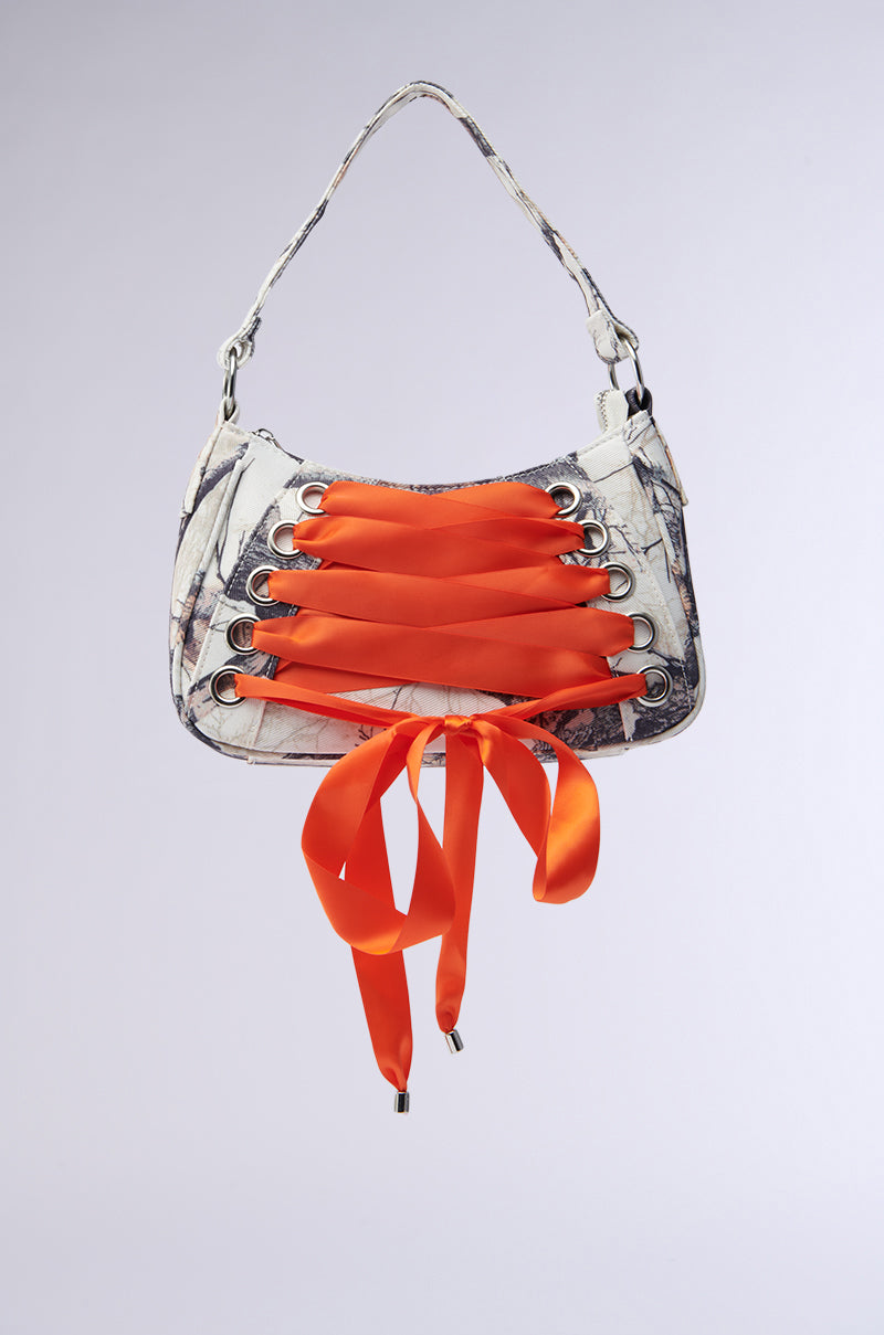 The CAN U SEE ME PURSE showcases a gray and white marble pattern akin to subtle camouflage, with bold orange satin ribbons threaded through metal eyelets on the front. Adjustable laces form a bow at the bottom, producing a striking contrast against its muted backdrop.