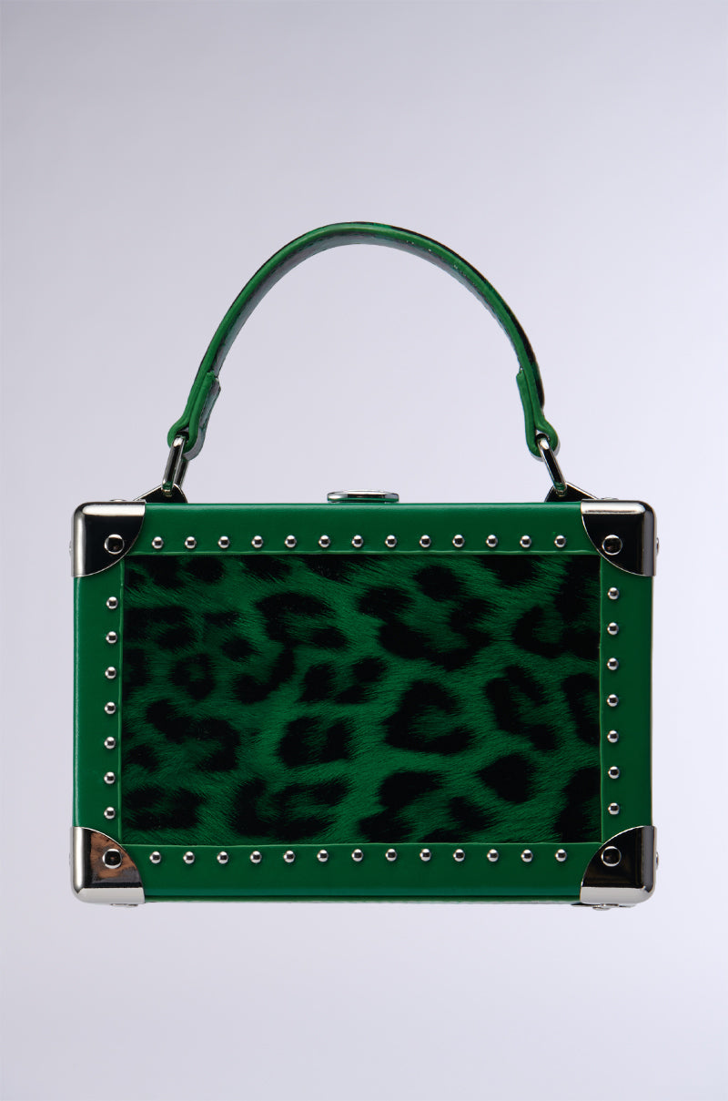Introducing the LIKE TO CHASE TRUNK PURSE: a small, rectangular handbag crafted from faux leather in an eye-catching dark green and black leopard print pattern. It is accented with silver studs around the edges and metal corner protectors, featuring a green handle attached to the top for a chic look. The bag also includes a detachable shoulder strap, providing you with versatile carrying options. Its background features a plain gradient, making it the perfect accessory to complement any outfit.
