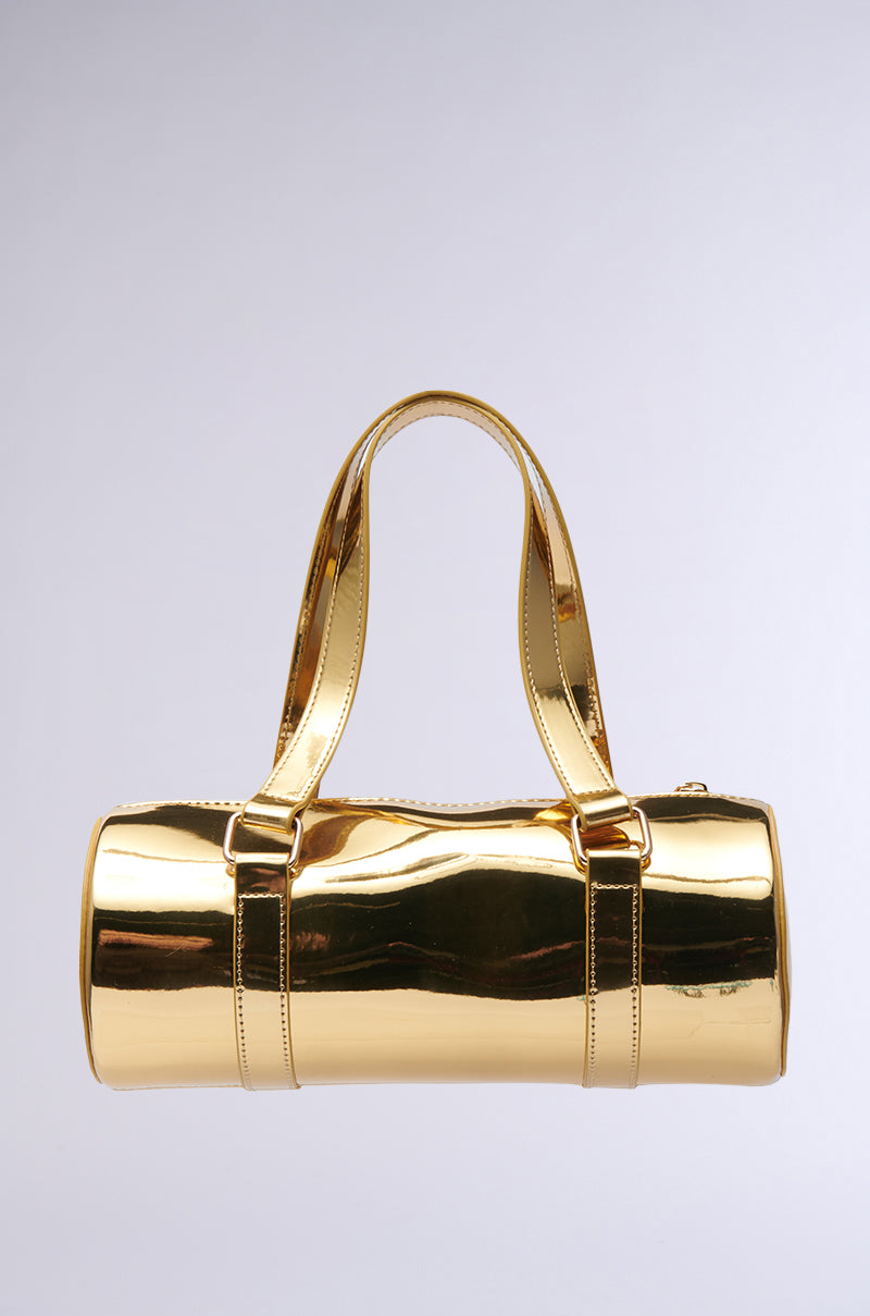 The CHROME DREAMIN PURSE, a shiny cylindrical gold handbag featuring a sleek barrel-style silhouette and two handles, floats against a plain gray background.