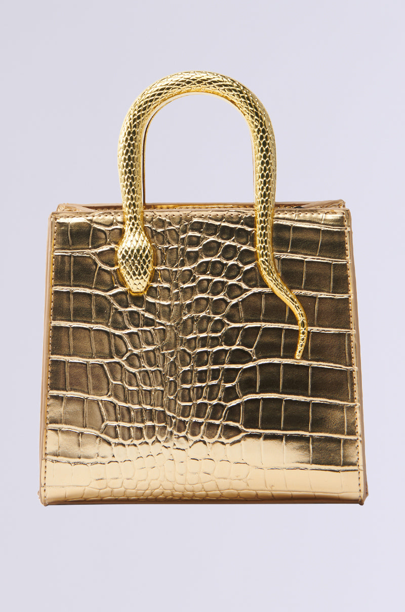 The SNAKIN THRU LIFE GOLD CHROME PURSE is a square gold chrome purse with a crocodile texture and a unique snake-shaped handle extending over the top, set against a plain, light background.