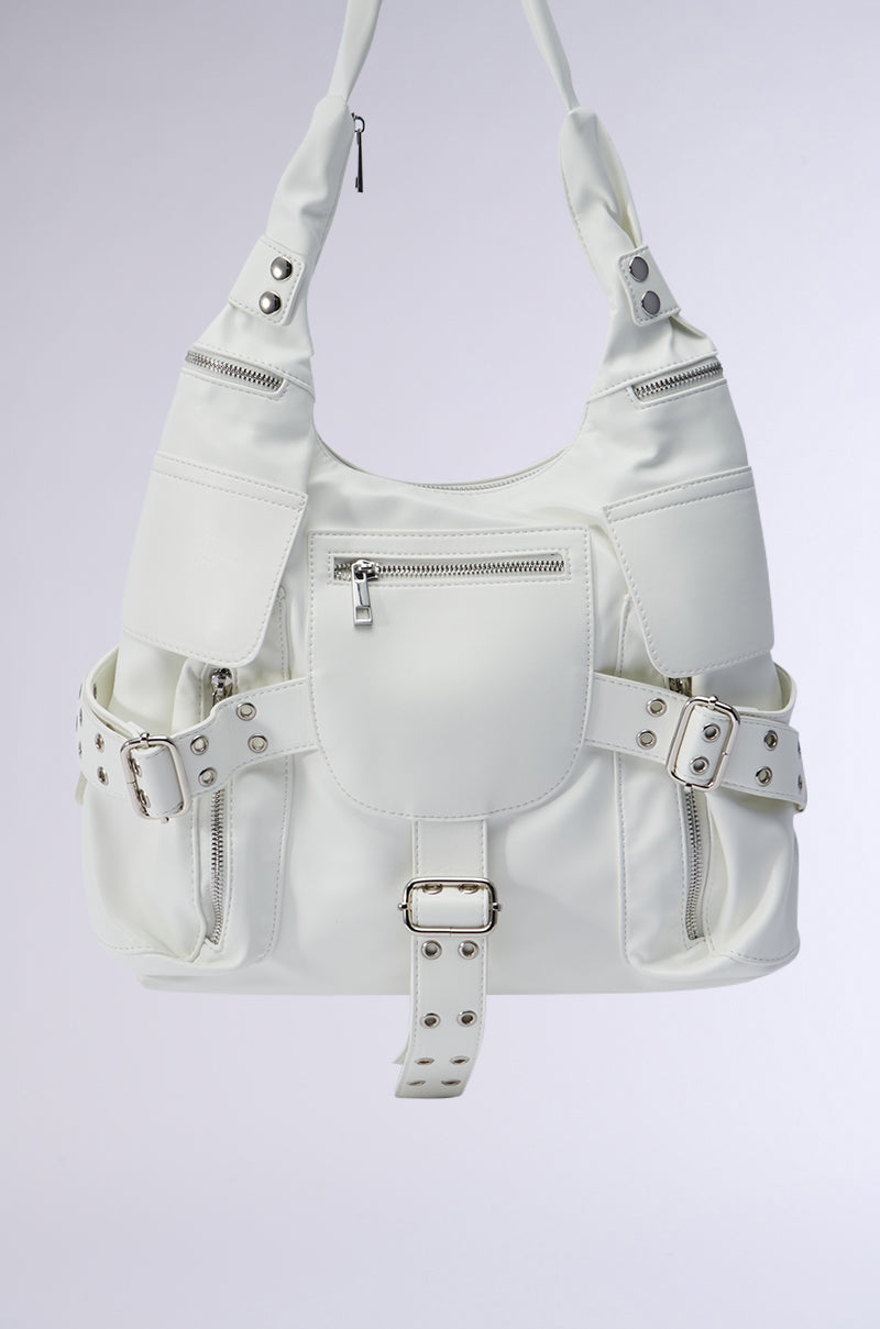 The R U WITH IT BAG is a stylish and roomy tote crafted from sophisticated white faux leather. It features multiple pockets and silver zippers, along with two decorative belts adorned with silver buckles and rivets. The bag includes a top handle for convenient carrying and an oversized design that makes it pop against a simple backdrop. 3