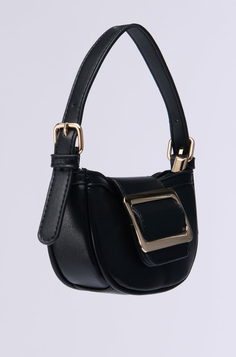 The QUIET LUXURY MINI PURSE exudes sophistication with its black faux leather design, complemented by a short strap and an oversized rectangular gold buckle on the front. Its polished gold hardware and soft, rounded shape create an elegant statement against a neutral background. 2
