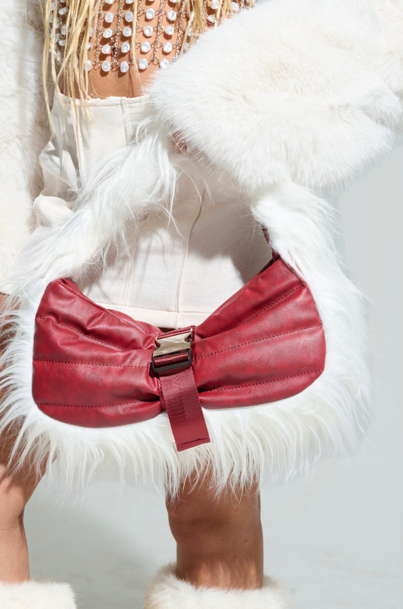 Clutching the OVERZEALOUS FUR TRIM PURSE, which features striking red leather and white faux fur accents, a person exudes the sophisticated style of the AKIRA Label. Dressed in an elegant white fur coat and a beige ensemble, they stand out against the plain, neutral background.