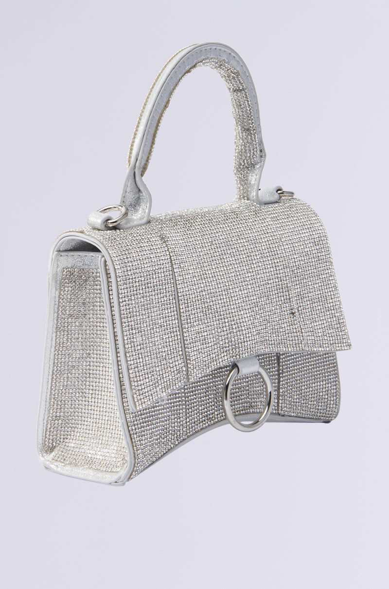 The BLING PURSE sparkles with silver rhinestones, a short handle, and flap closure featuring a round metal detail. Set against a plain light gray background, this handbag exudes elegance and charm. 2
