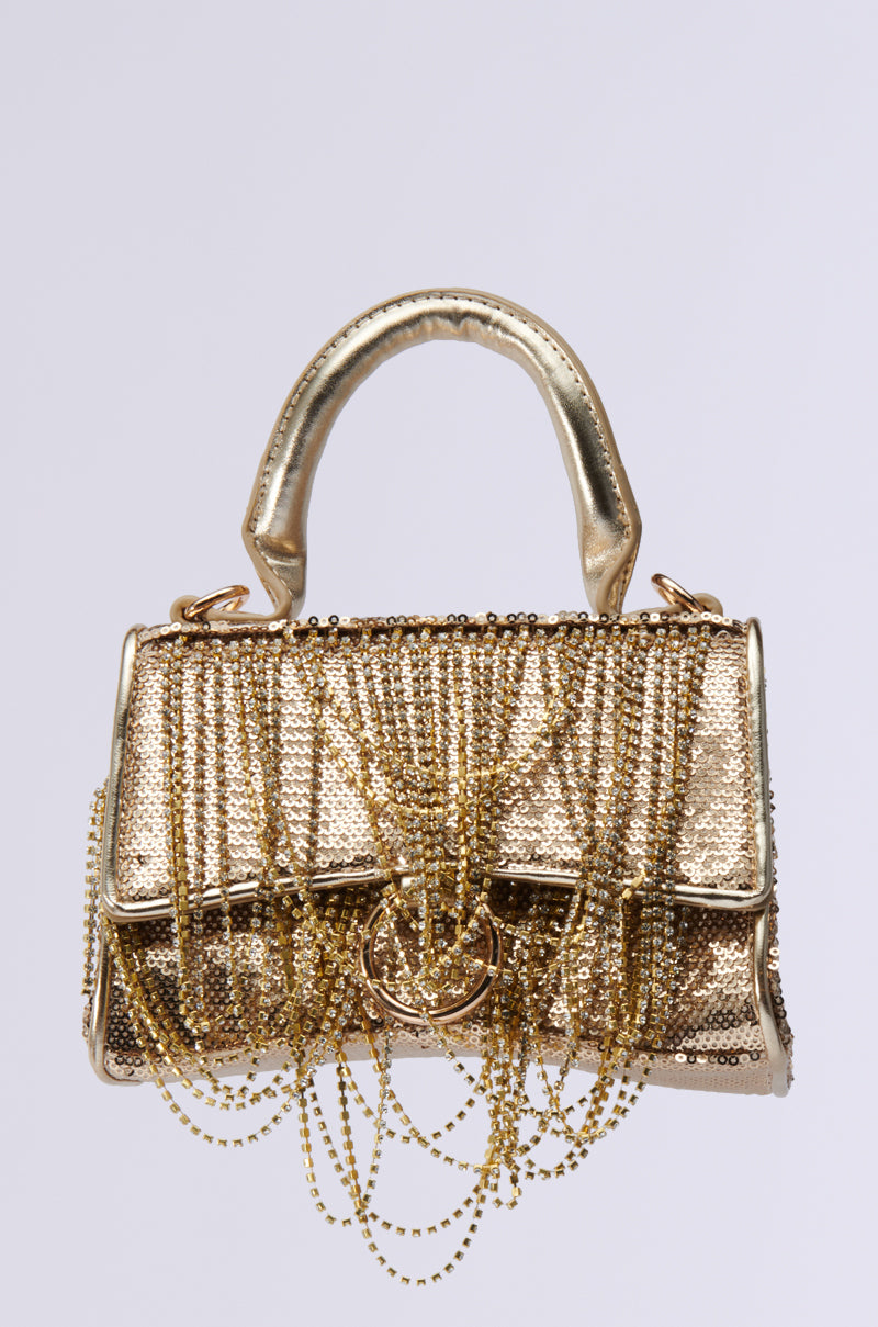 The KEEP DREAMING BLING PURSE is a luxurious gold evening bag embellished with shimmering beads and features rhinestone fringe and chains. It has a textured surface and a sturdy handle, creating an intricate design for an elegant, sophisticated appearance.