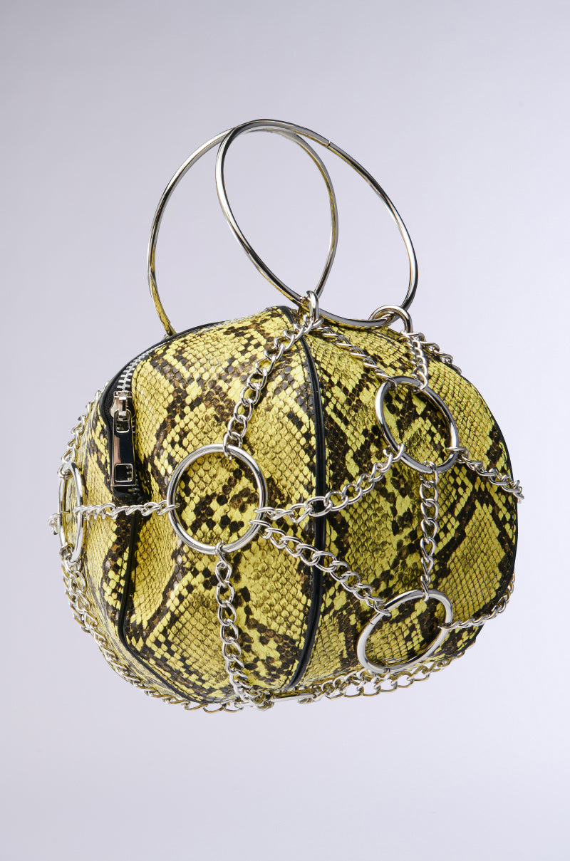 The MY STANDARD SNAKE BAG is a spherical handbag made from vegan leather, featuring an eye-catching yellow and black snakeskin pattern. It is embellished with silver chains and large rings, with a top handle crafted from elegant silver loops for a chic finish. 2