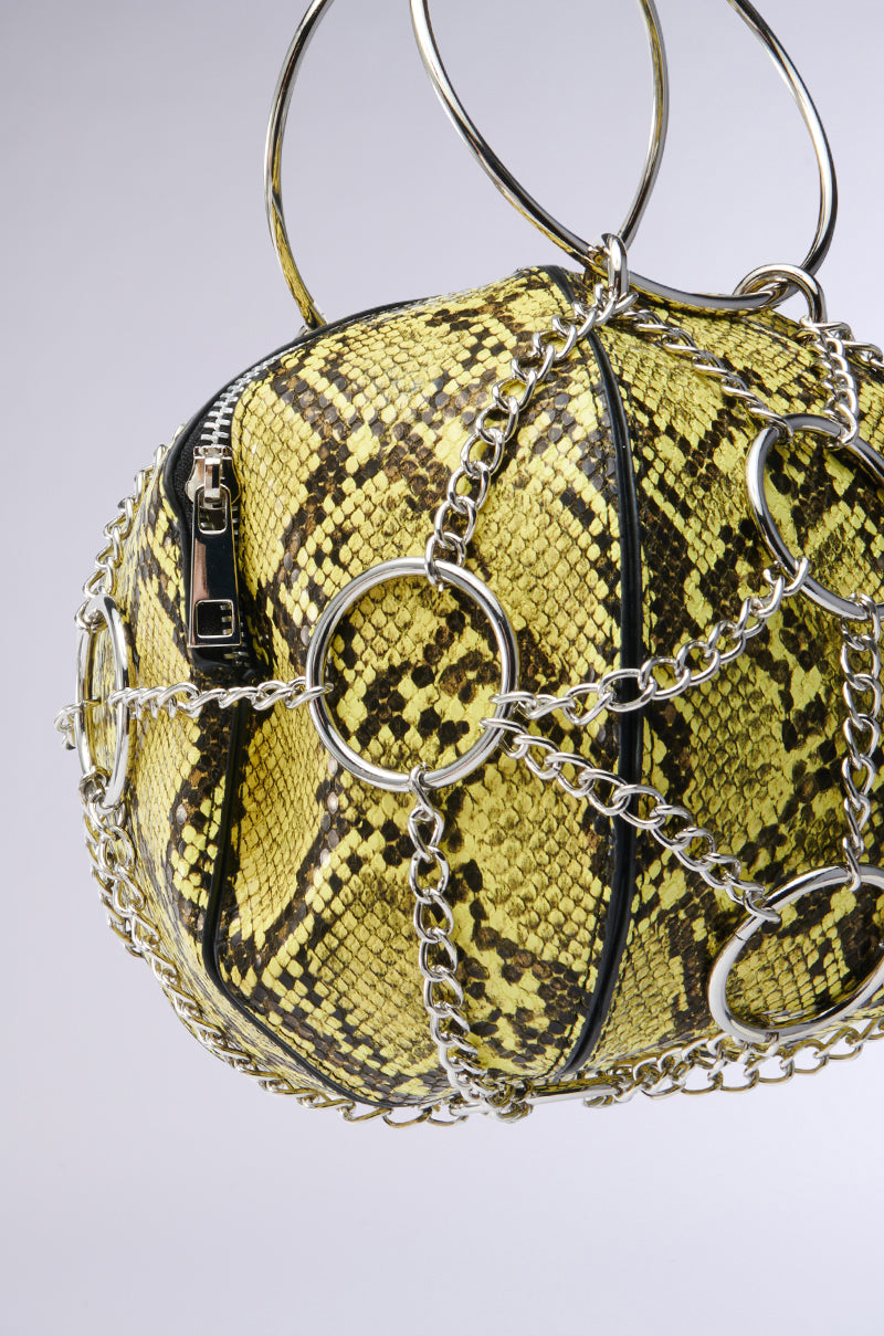 The MY STANDARD SNAKE BAG features a yellow and black snakeskin pattern on vegan leather, encased in a silver chain web with circular rings creating a geometric design, set against a gray background for an edgy look. 3