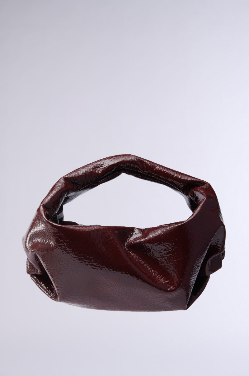 The LEATHER LOVIN' PU PURSE IN BURGUNDY is a glossy, chic handbag with a unique, irregular shape set against a light gray background. Crafted from faux leather, it features a soft, crumpled appearance with an open top. 0