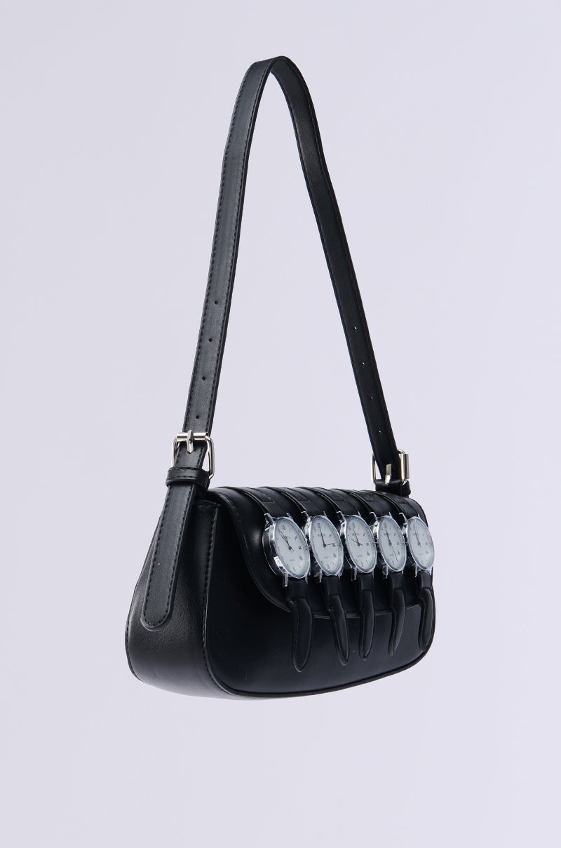 The WATCH YA SELF PURSE is a chic shoulder bag made from black vegan leather. It features five analog watch faces as embellishments, with an adjustable buckle strap. Set against a light gray background, this piece makes a bold statement.