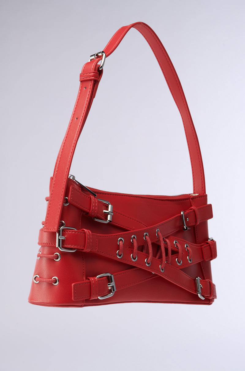 The CROSSED OUT SHOULDER PURSE is a red vegan leather handbag with distinctive crisscross straps, metal eyelets, and buckles. It features a wide, adjustable strap and exudes a modern, edgy style. 4
