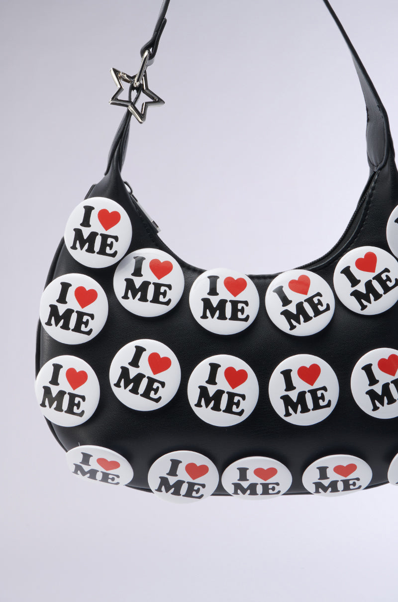 The I REALLY DO PIN PURSE, in black faux leather, is a chic accessory featuring "I ♥ ME" badges. A playful star-shaped charm on the strap adds flair, and its soft gray background showcases the AKIRA Label's bold design style.