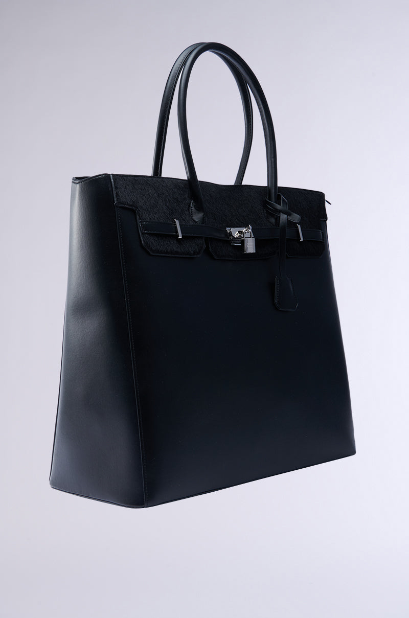 The FEEL ME OVERSIZED TOTE in black faux leather, featuring double handles and silver hardware with a small front lock, showcases a sleek, structured shape against a plain background. Its spacious interior adds practicality to its elegant design.