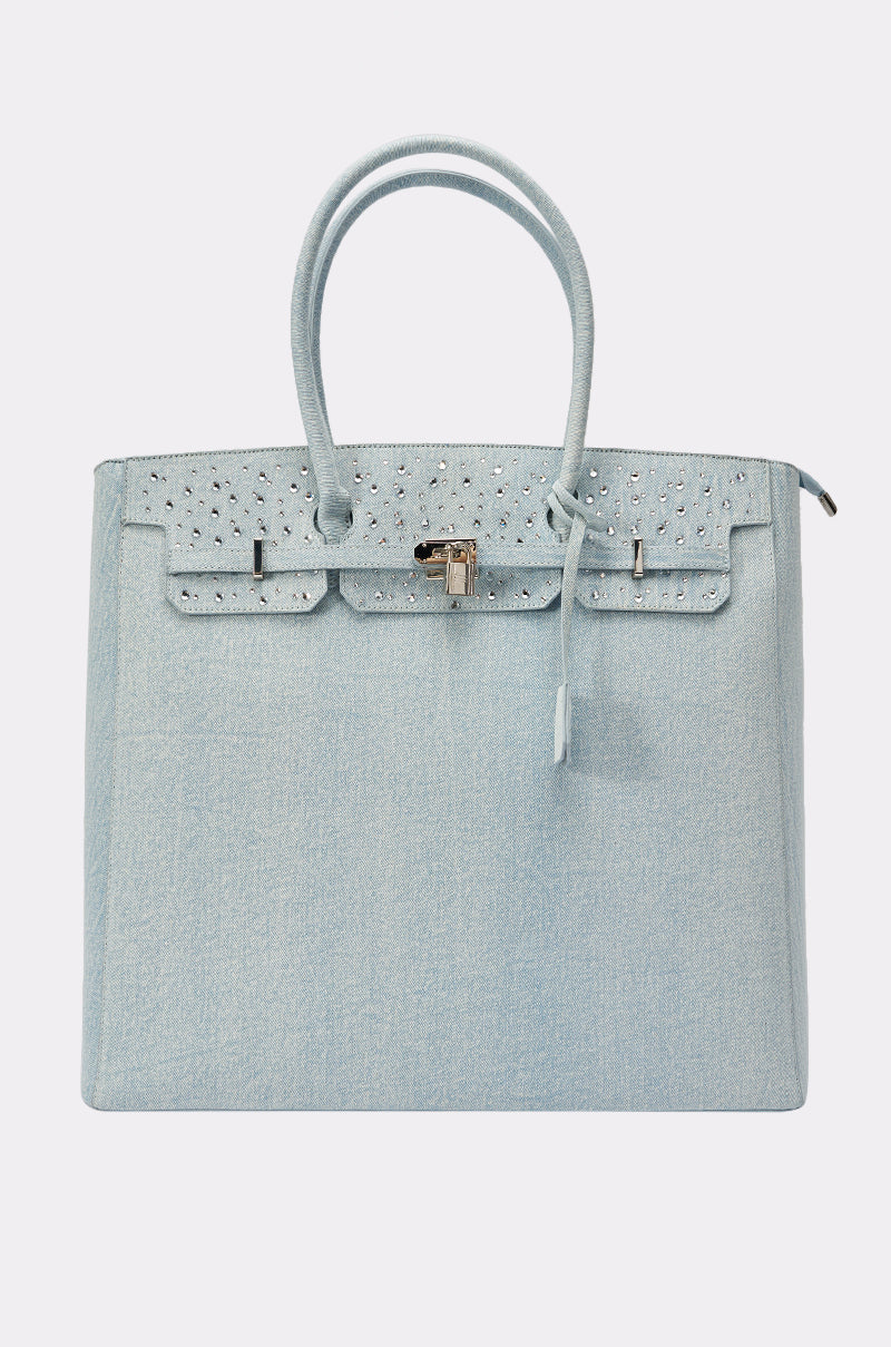The DENIM AND DIAMONDS OVERSIZED TOTE is a pastel blue handbag with rhinestone embellishments, dual handles, a textured finish, and a flap with a silver lock and studs, set against a light gray background. 3