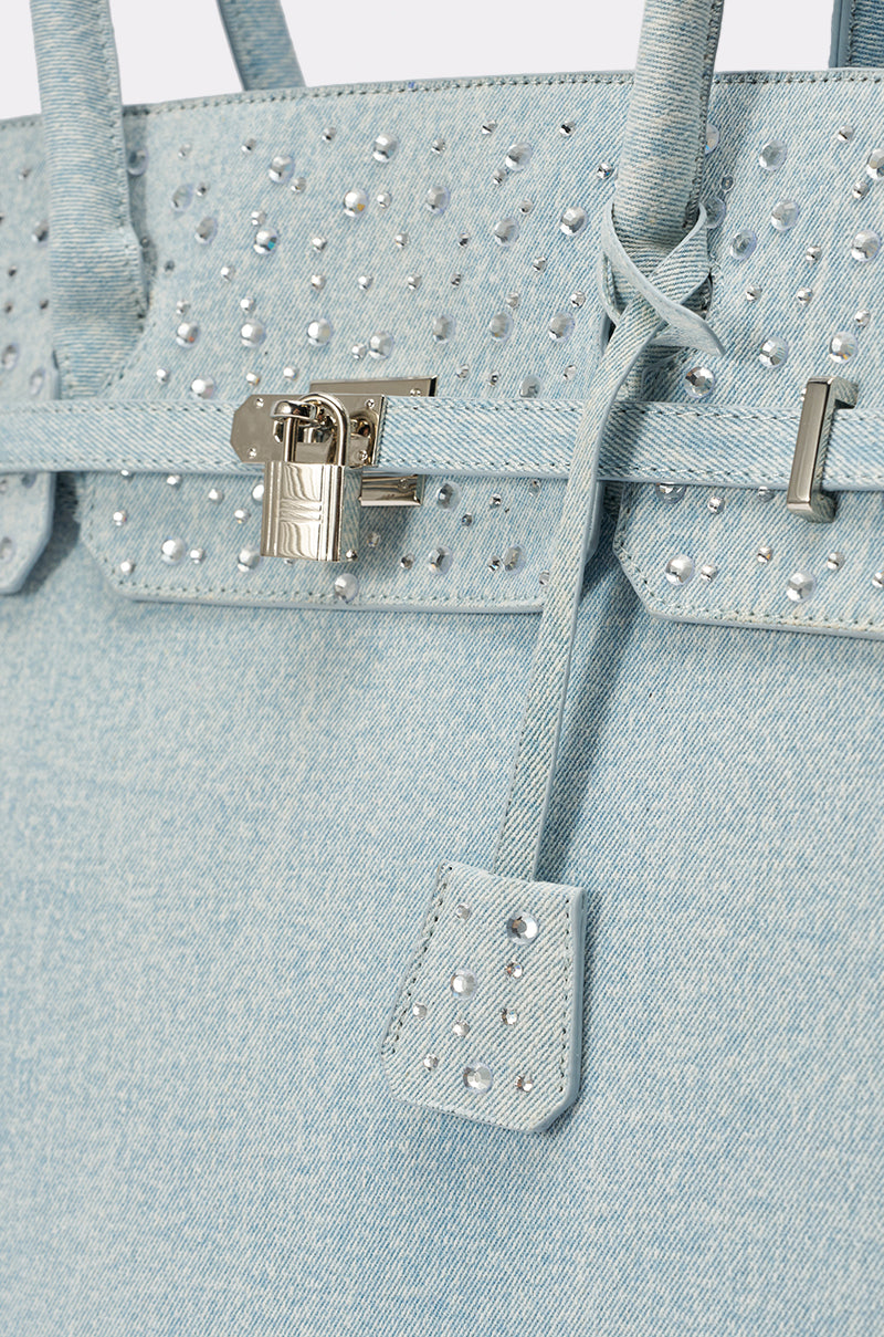 Close-up of the DENIM AND DIAMONDS OVERSIZED TOTE: a light blue, bedazzled denim bag with silver studs, a silver lock and hardware, double handles, and a matching leather tag detail. 5