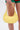 A person in green and red shorts holds a yellow GET WITH THE TREND PU PURSE with a short handle against a plain white background.