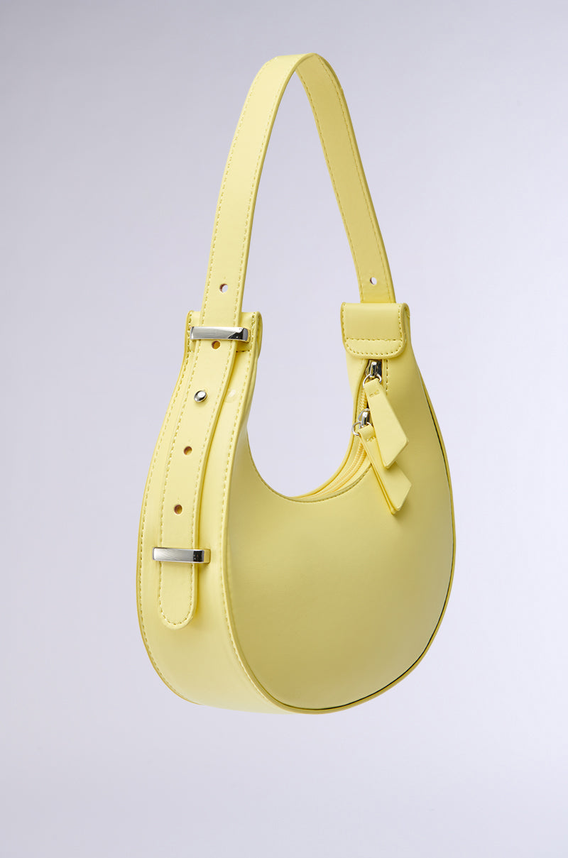 The GET WITH THE TREND PU PURSE features a stylish pastel yellow crescent silhouette, adjustable strap, silver hardware, and a small tag, showcased against a plain light gray background.